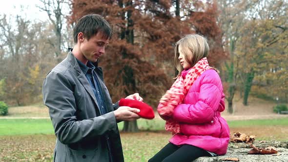 Dad putting red cap on daughter's head and scarf in the park