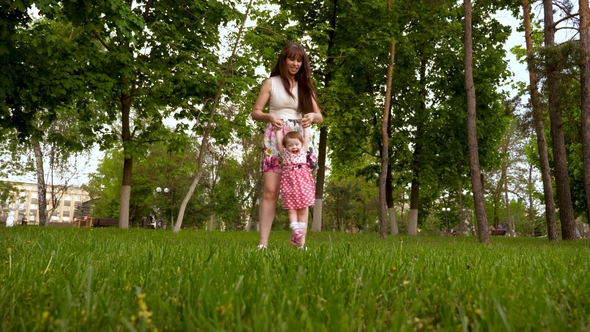 Mom Is Shaking Hands in Air with a Happy Laughing Daughter. Parent Plays with Baby on Green Grass in