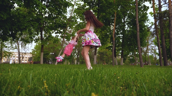 Mom Is Circling Hands in Air with a Happy Laughing Daughter. Parent Plays with Baby on Green Grass