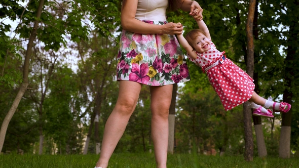 Mom Is Shaking Hands in Air with a Happy Laughing Daughter. Parent Plays with Baby on Green Grass in