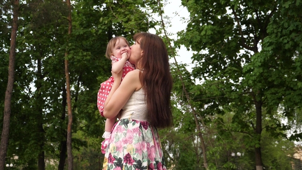 Mom Holds an Infant in Her Arms and Laughs in a Warm Green Park