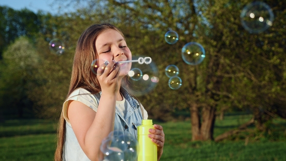 Happy Child Blowing Soap Bubbles in Spring Park