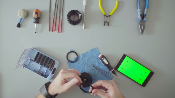 Hands with Screwdriver and Tweezers Repair Lens