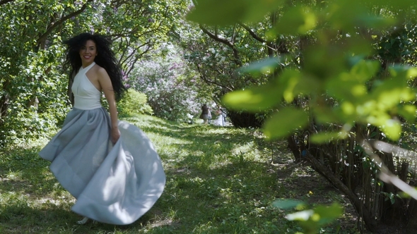 Charming Brunette Moves Her Long Dress Standing in a Green Garden