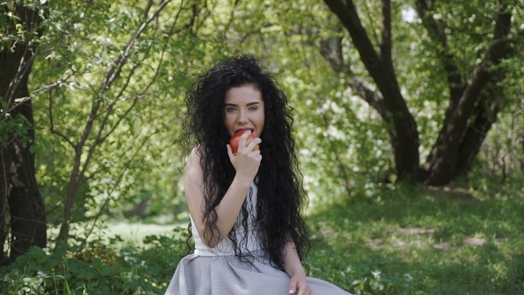 Beautiful Woman Eat Fresh Apple Sitting in Summer Garden