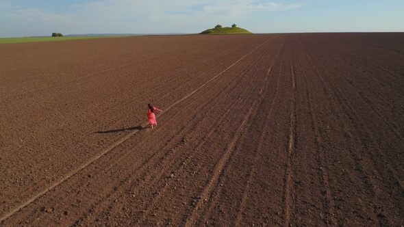 Carefree Woman Wearing Long Red Dress Walking on the Plowed Field