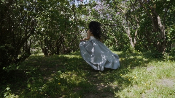 Beautiful Brunette in Long Blue Dress Run Through a Garden