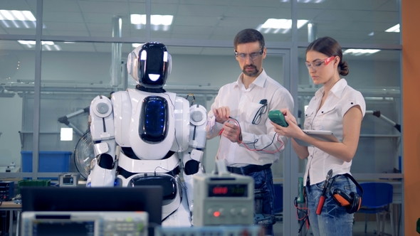 Male and Female Engineers Are Taking Readings of a Human-like Robot with Special Equipment