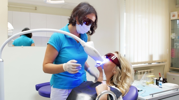 Dentist Talking to Patient Lying in Dentist Chair during Teeth Whitening Procedure