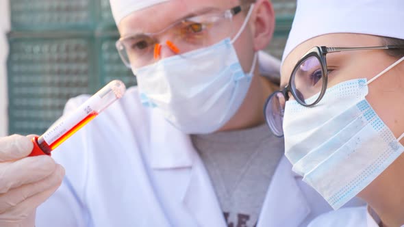 Two Doctors Exploring Test Tube with Blood Sample To Coronavirus. Male and Female Medics with