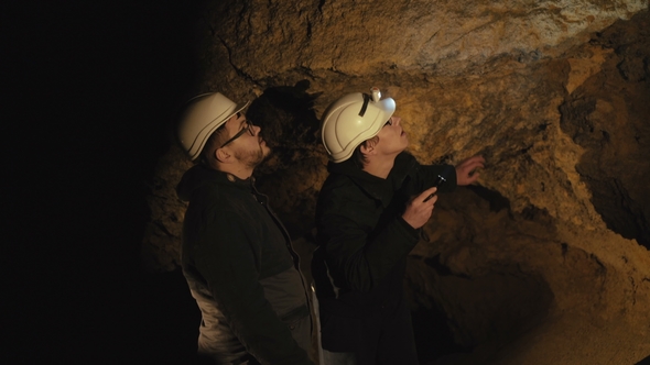 Two Speleologists with Flashlight Exploring the Cave with Fear in Darkness