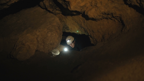 The Speleologist Finds and Goes in Passage in the Cave.