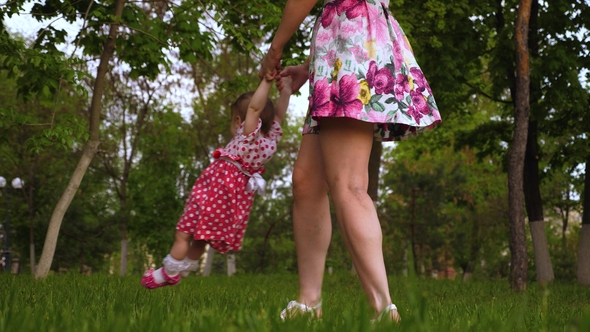 Mom Is Circling Smiling Baby in Her Arms in Air. Little Child Is Playing with Parent in Green Park