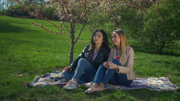 Two Adorable Diverse Girls Resting in Blooming Park
