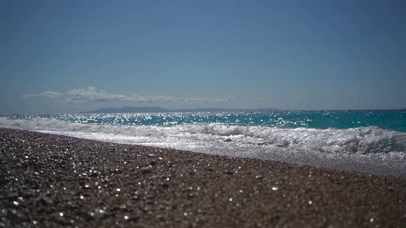 Stone Sea Shore in Sunny Day with Waves Lapping on Beach and Forming White Foam