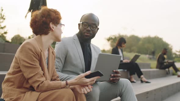 Diverse Colleagues Using on Laptop and Having Discussion Outdoors