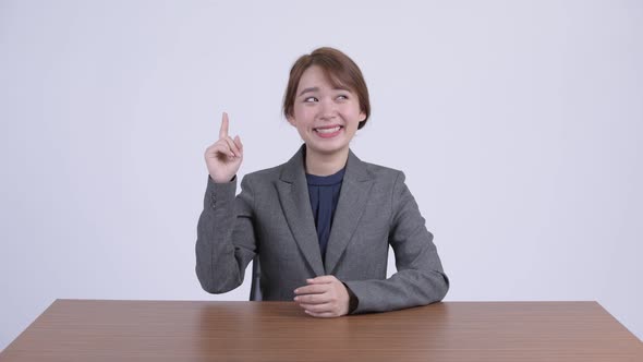 Young Happy Asian Businesswoman Thinking and Pointing Up at Desk