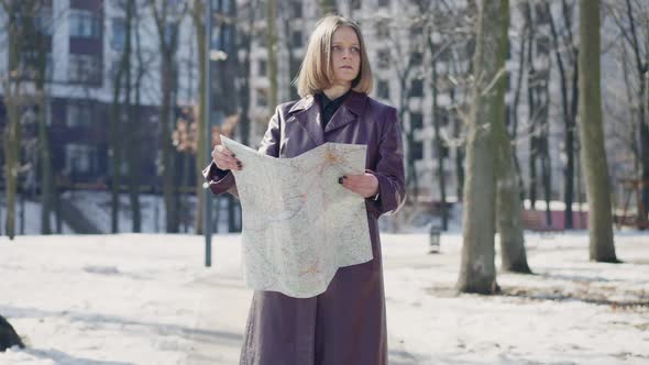 Portrait of Unsure Caucasian Female Tourist with Paper Map Standing in Winter Town Looking Around