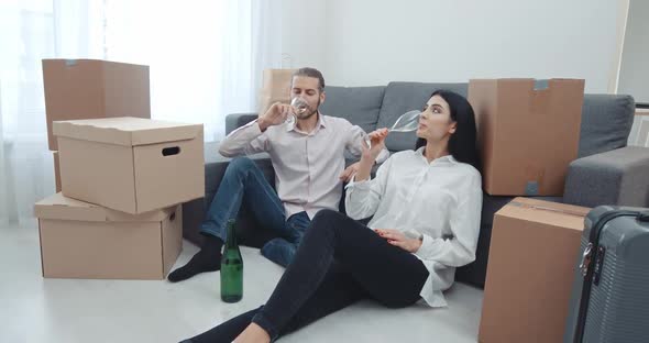 Moving To a New Apartment, a Young Couple Sitting on the Floor Near Boxes of Things and Drinking