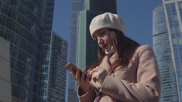 Woman with the Phone on the Background of High Buildings of a Megacity
