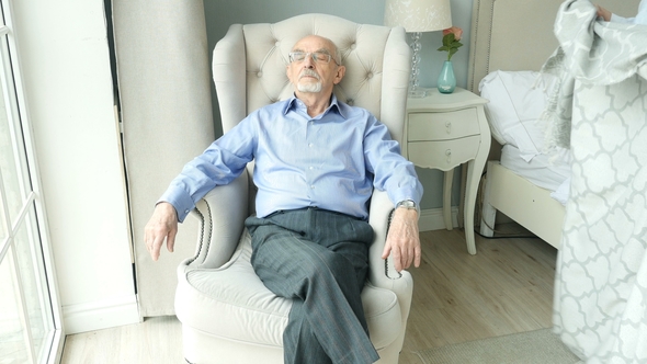 Elderly Man Sits on a Chair By the Window and Sleeps