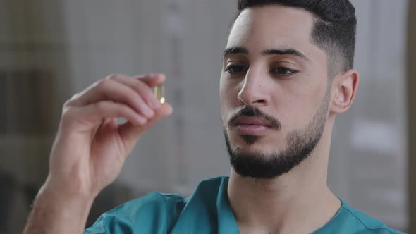 Young Scientist Hispanic Man Medical Employee Holding Clear Transparent Capsule Tablet in Hand