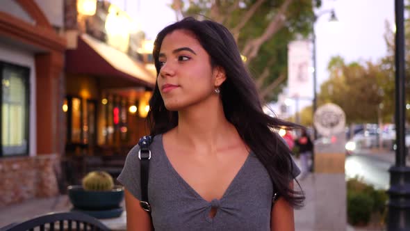 A beautiful hispanic woman walking a downtown urban city street looking in restaurants, shops and re