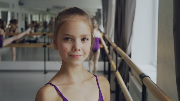 Portrait of Beautiful Little Girl in Bodysuit Standing in Ballet Class, Smiling and Looking