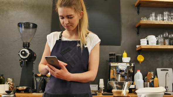 Delighted Female Barista Using Cell Phone at Work Place