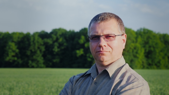 Portrait of a Successful Farmer, Looking at the Camera. Against the Background of a Green Wheat