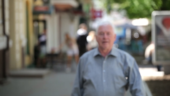 Confident Grey-headed Man Goes in a Green Street on a Sunny Day in Summer