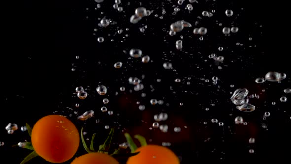 Closeup of fresh and health cherry tomatoes falling into clear water with big splash 