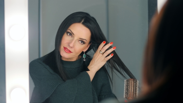 Pensive Beautiful Woman Wearing Green Clothes Is Looking at Her Reflection in Mirror and Combing Her