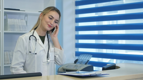 Pretty Nurse Using Tablet and Phone at Hospital Reception Desk