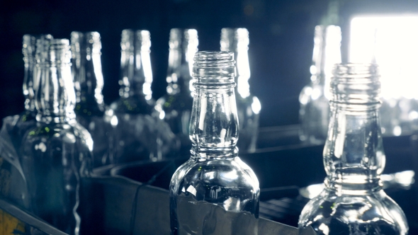 Empty Glass Bottles with Ribbed Necks Are Moving in a Row Along the Conveyor Belt