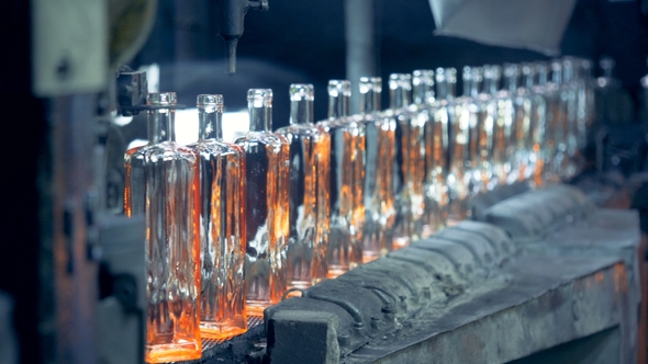 A Line of Incandescent Newly-made Glass Bottles Is Moving Along the Conveyor Belt