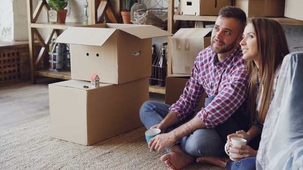 Cheerful Young Woman Is Talking To Her Husband About Their New House Sitting on Floor During