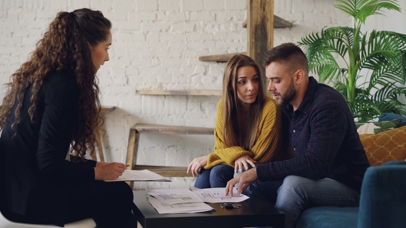 Side View of Young People Real Estate Agent and Buyers Looking at House Plan Sitting at Table in