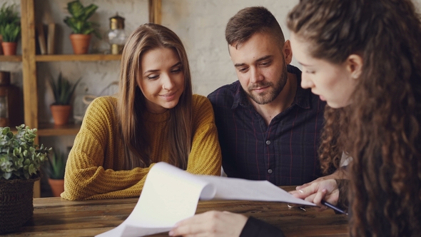 Female Realtor Is Reading Purchase and Sell Agreement To Young Couple, Man Is Signing Document and