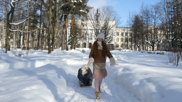 Ginger-Haired Little Girl Walking on Winter Park at Sunny Day and Sledding Her Toy