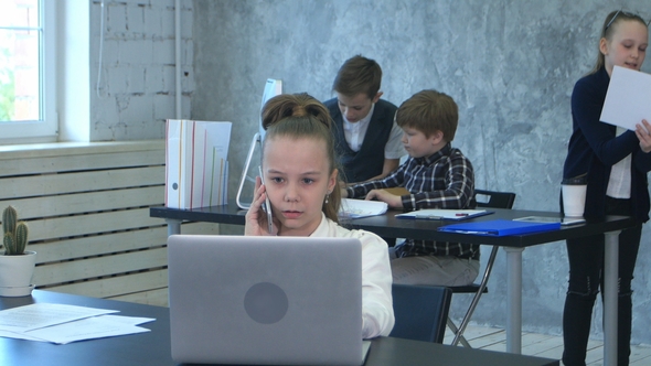 The Kids Discuss Project in Office, While One Business Girl Talking on Phone