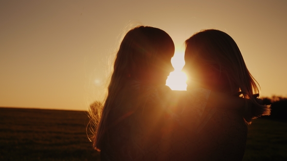 A Woman with a Daughter in Her Arms. Gentle Looking at Each Other, Silhouettes at Sunset