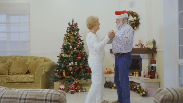 Mature Man Wearing Santa Hat Dancing with Wife at Home Near Christmas Tree