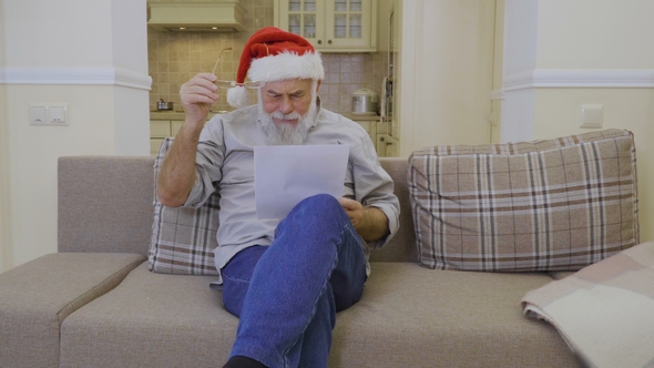 Senior Man in Santa's Hat Reads Family Wish List on Christmas