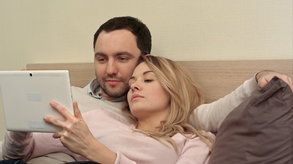 Young Couple Lying on the Bed Make Shopping Over the Internet Using Tablet Using Tablet Computer