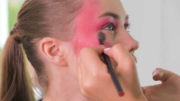 Makeup Artist Making Beautiful Face Art for Young Blonde Woman with Makeup Brush