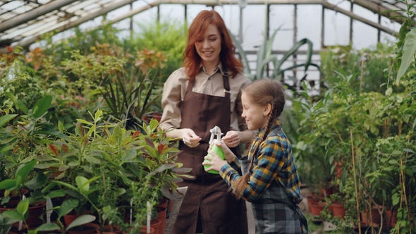 Young Woman and Her Daughter Are Sprinkling Water on Flowers, Child Is Having Fun and Spraying Her