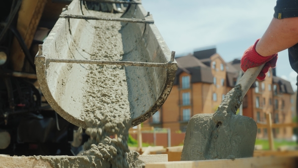 Building a Cottage. Workers Take Concrete From a Mixer Into a Wooden Formwork