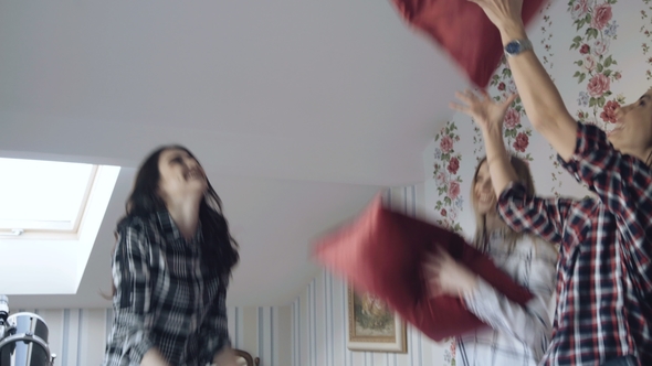 Three Young Pretty Girls Jumping on Bed and Fight Pillows Having Fun at Home