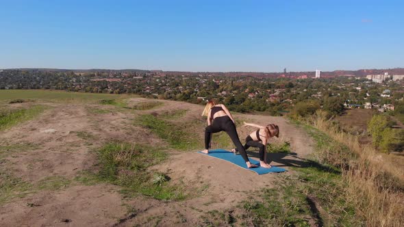 Aerial Drone View of Slender Young Mother Do Yoga Exercises with Child Daughter on High Hill By Lake